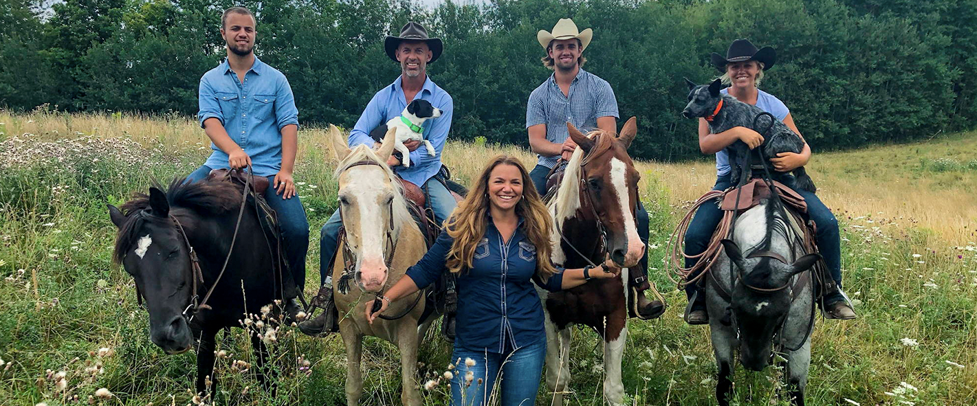 4 people on horses and a person standing in front of them in a field