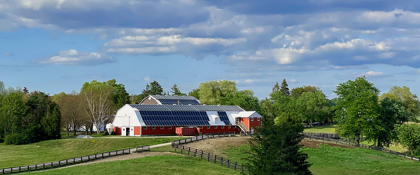 red barn with solar panels on the roof in the distance of a large green field