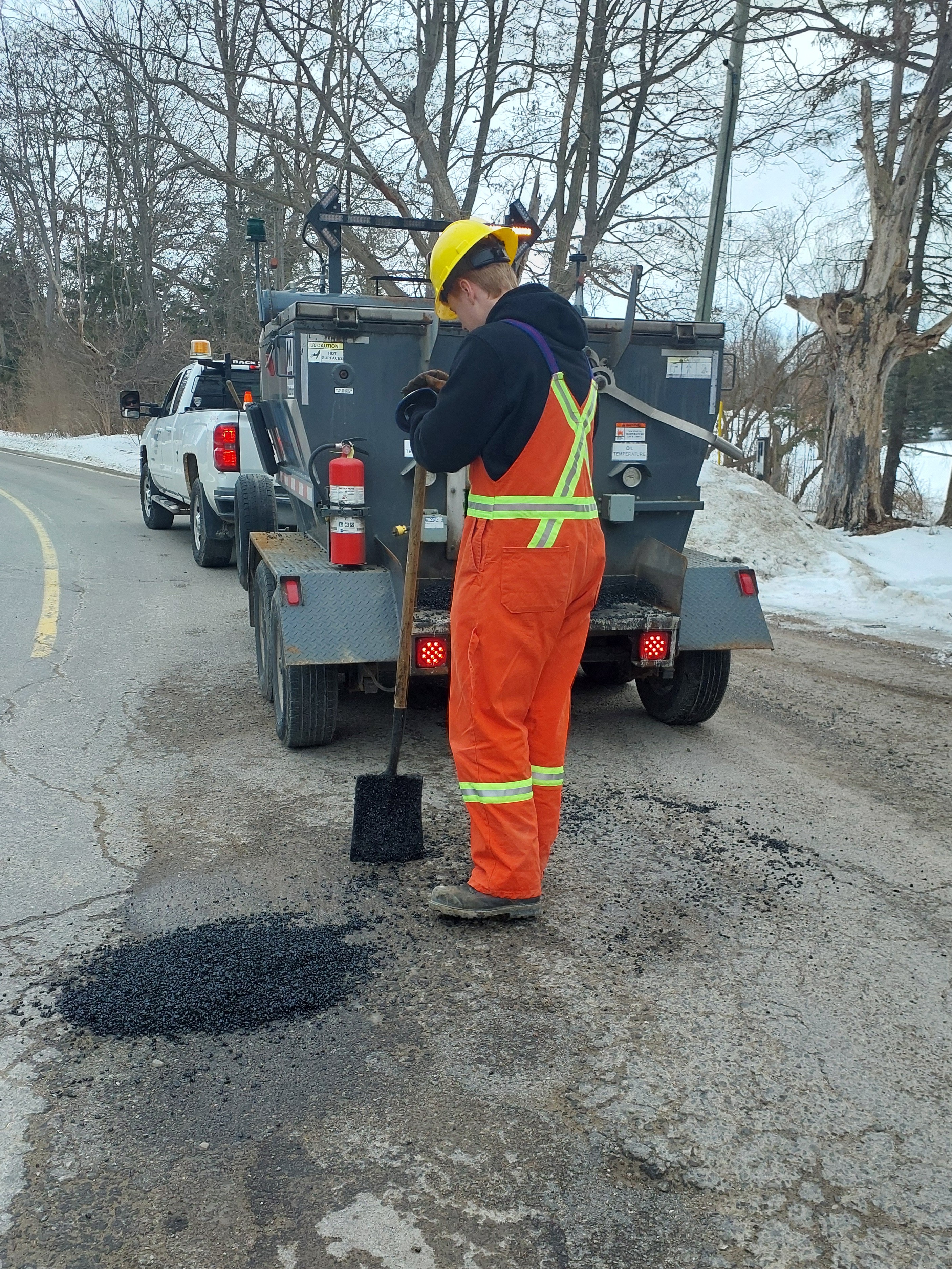 Roads crew member wearing safety gear filling in a pothole