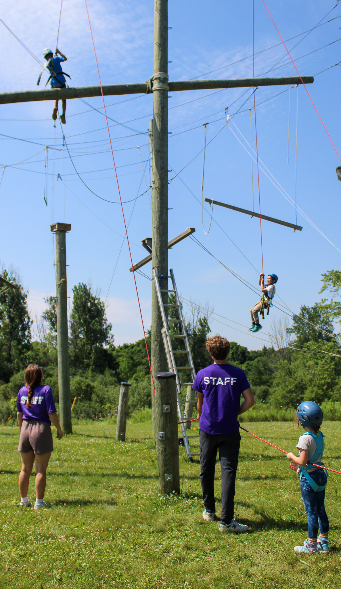 Two camp counsellor staff members assisting a group of children on high ropes course