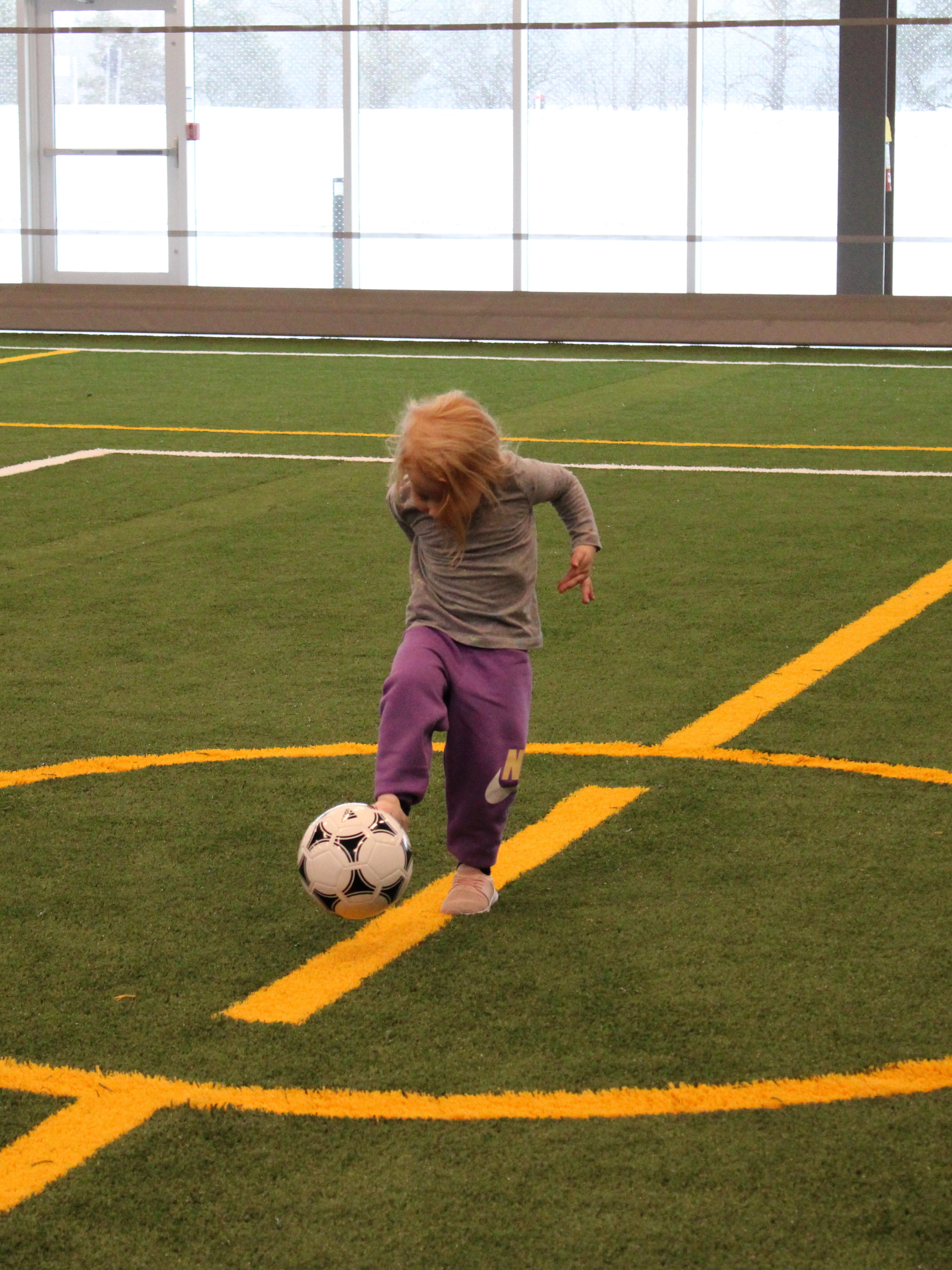 Child kicking soccer ball on indoor green turf