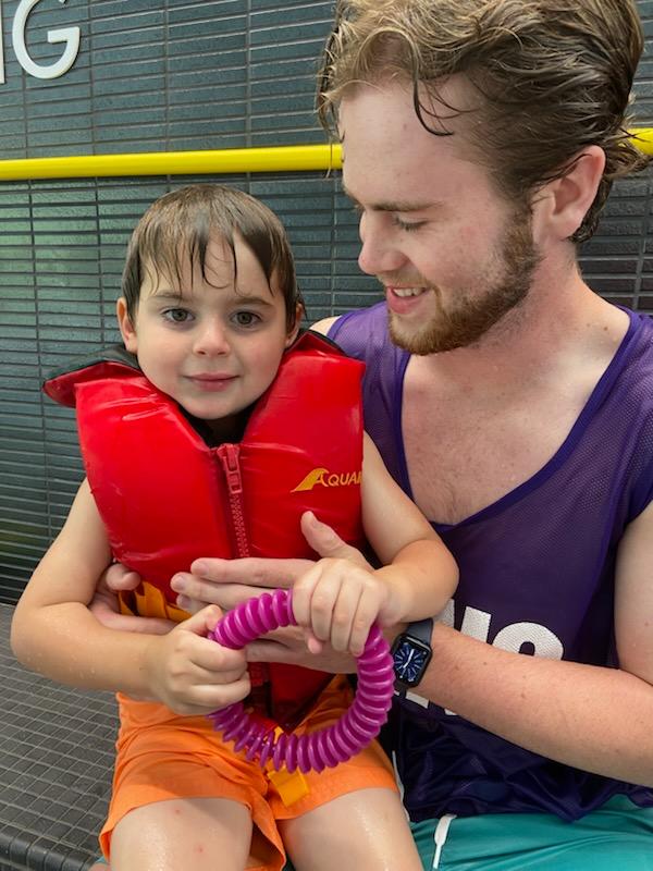 Staff member and camper posing together by side of the pool, smiling