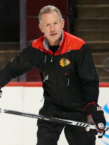 Image of Mike Kitchen skating on the ice with a hockey stick in coaching attire