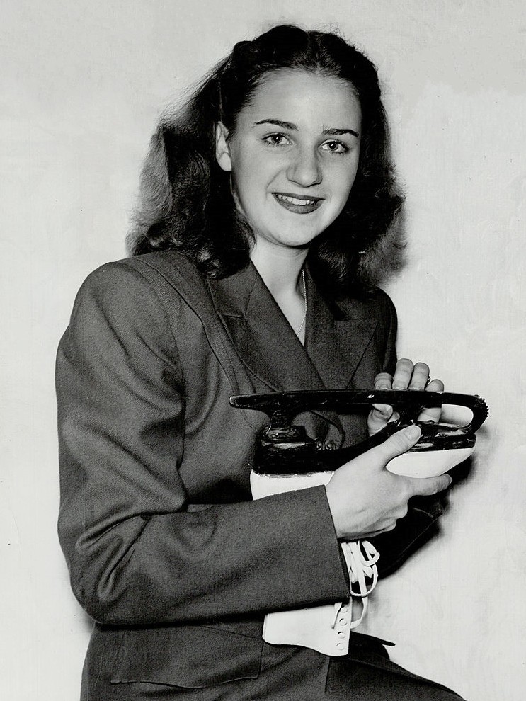 Black and white image of Suzanne Morrow (Francis) smiling holding a white figure skate