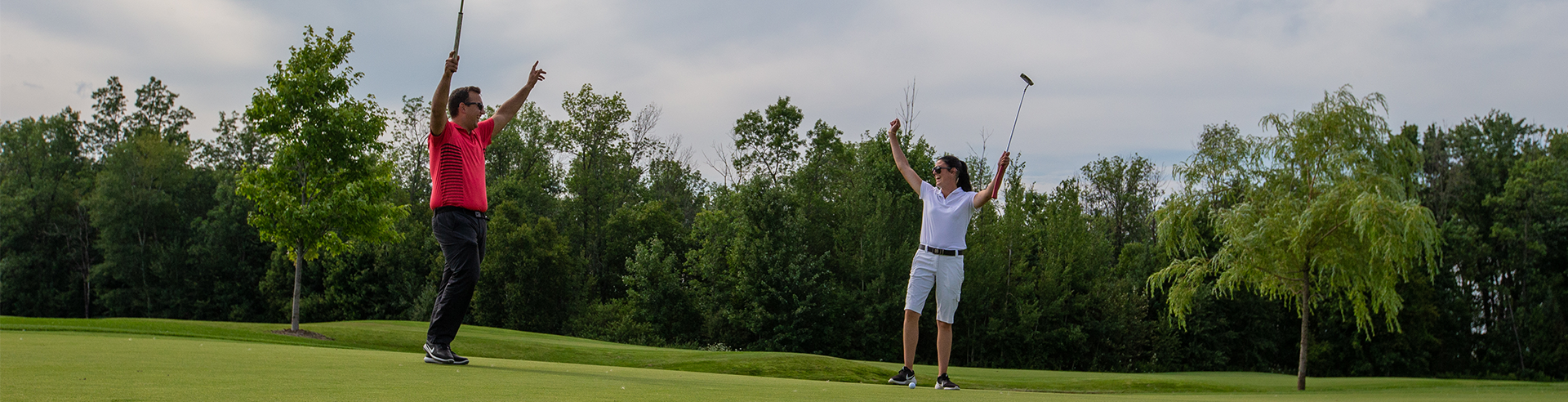 Two people cheering on the golf course with golf clubs in the air at Cardinal Golf Club