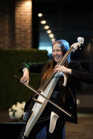 Person playing the cello, smiling in an elegant venue backdrop with flowers and exposed brick